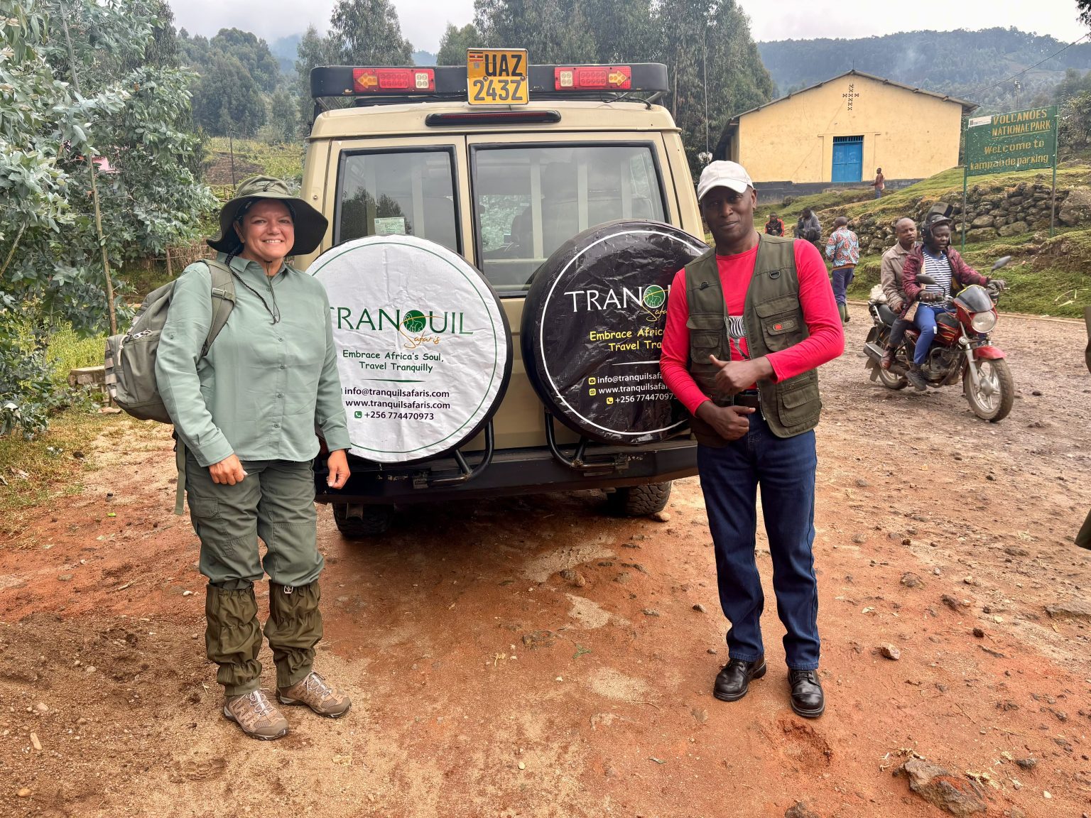 A traveller and a Tranquil Safaris guide standing behind the company Land Cruiser on a village road, with people passing on a motorcycle behind them.