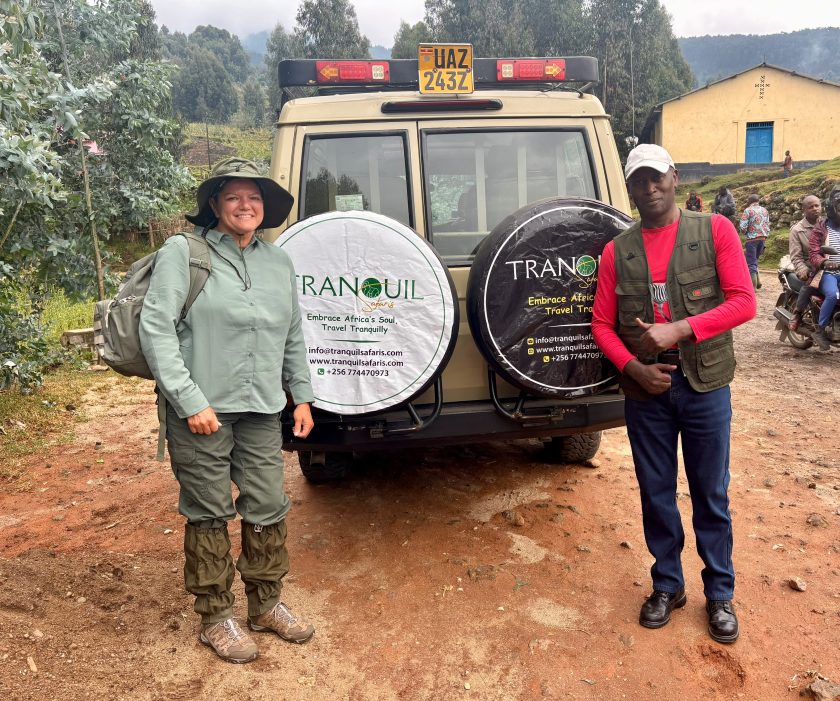 Godwin, a senior Tranquil Safaris guide, standing with a traveller either side of a company four-wheel-drive on red earth, its spare-wheel cover printed with the company name and contact details.